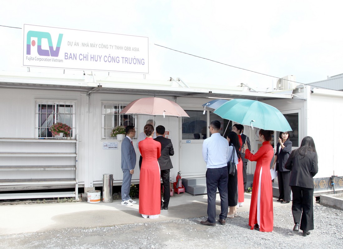 PG cầm ô hỗ trợ khách mời di chuyển tại khu vực văn phòng công trường.