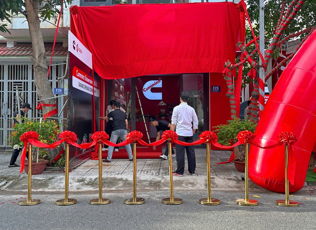 Nhân sự chuẩn bị khu vực nghi thức trước showroom Cummins với màn phủ đỏ và dải băng.
